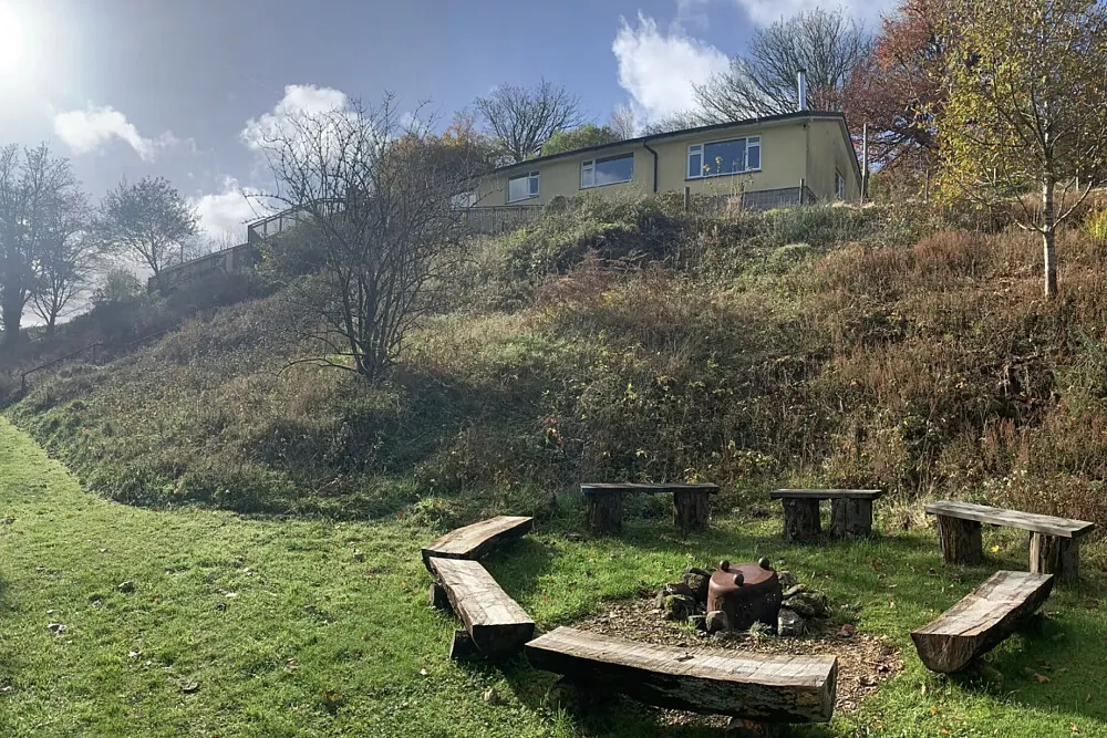 The main building at High Heathercombe above a fire circle of log benches, near Manaton on Dartmoor